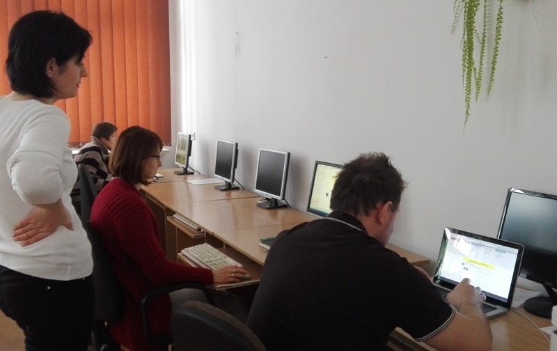 Nauczyciele pracują na komputerach, obok stoi pani prowadząca szkolenie.