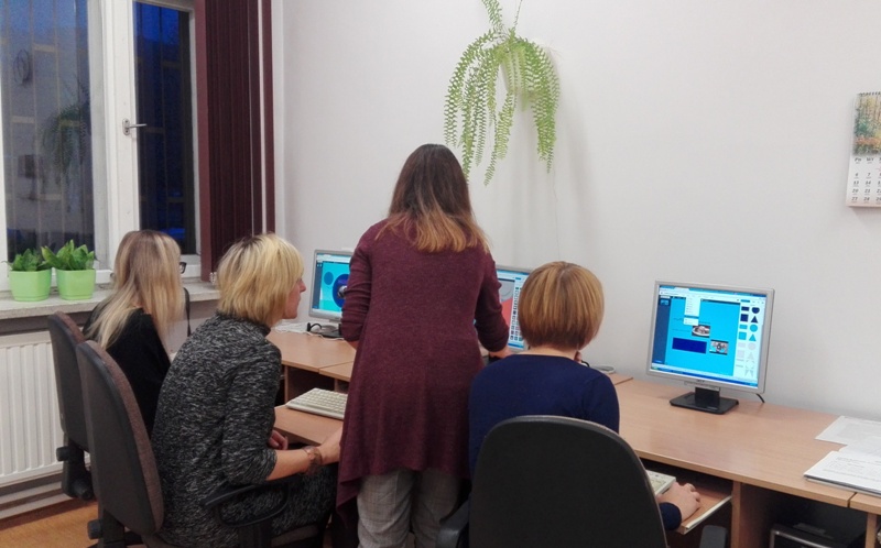 Nauczyciele pracują na komputerach, obok stoi pani, która wyjaśnia działanie aplikacji.