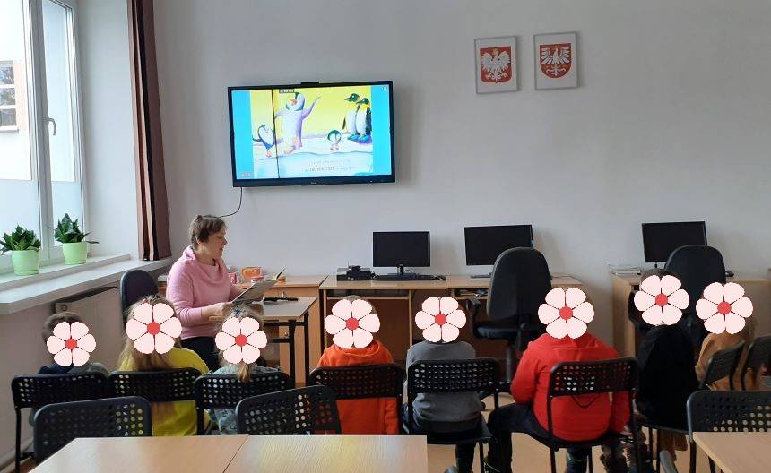 Zajęcia czytelnicze dla dzieci. Dzieci słuchają jak pani bibliotekarka czyta książkę.